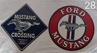 Two metal Ford Mustang signs laid flat on a white background showing one diamond-shaped and one round sign with Mustang logos.