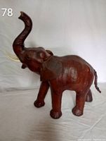 Full side view of the brown elephant statue with raised trunk showing the right side, tusks, and tail.