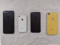 Four iPhones laid side-by-side showing back view: yellow phone with cracked screen, white phone, two black phones.