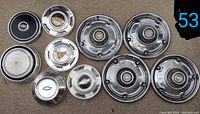 10 hub caps placed on ground with various designs and sizes, mostly Chevrolet logos visible