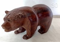 Side view showing the full body of the ironwood bear sculpture with its polished rounded back and detailed carved face and legs.