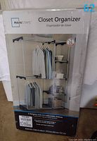 Front of box showing assembled closet organizer with clothes and boxes on shelves, with Mainstays brand name, product name, and a sticker with item number 62.