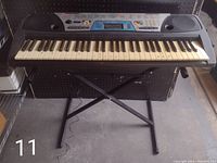 Front view of Yamaha PSR-170 keyboard on black X-style stand in a warehouse setting, powered by mains cable.