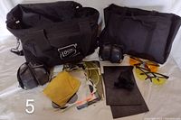 Shooters bag with accessories displayed including carrying cases, shooting glasses, earmuffs, foam mats, and a holster pouch.