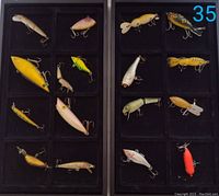 Two black display trays containing a total of 17 assorted multi-jointed fishing lures with treble hooks, showing diversity in size, color, and shape.