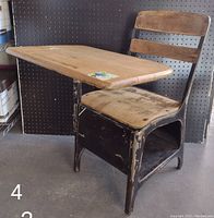 Side angle showing wooden desk top, metal frame with paint chipping, wooden seat and backrest with two horizontal slats.
