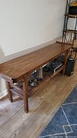 Side view of the long wooden console table showing the smooth top surface, side supports, and rattan shelf underneath with items stored.