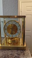 Front view of clock showing brass frame, glass panels and circular dial with gold-tone numerals.
