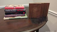 Stack of four hardback books on a wooden surface alongside four wood and metal bookends.