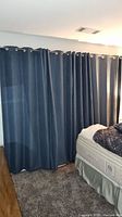Four dark blue blackout curtains hanging from brushed nickel grommets across window near bed, showing linen-style blackout polyester fabric and size.