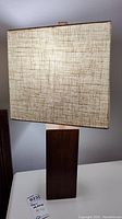 Close-up photo of one lamp showing wood rectangular base and beige linen shade texture.