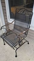 Side angle photo of the black wrought iron patio chair showing mesh seating and rust on armrest.