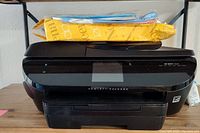 Front view of black HP Envy 7645 printer with papers and packaging on top.