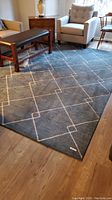 Blue area rug with geometric pattern placed in living room with furniture around.
