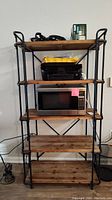 Front view of five tier shelving unit with wooden shelves and black cast iron frame, showing included items on shelves (contents not included in sale).
