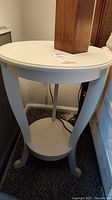 Overall view of round off-white painted wooden side table with two tiers and curved legs.
