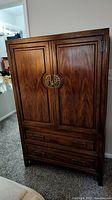Front view of Asian style wooden wardrobe with two doors and five drawers, decorative circular metallic handle.