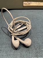 Photo of Apple white wired EarPods laid on blue fabric with cable partially coiled and two earbuds visible, including 3.5mm audio jack.