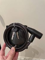 Photo showing the coiled cable lock with two keys attached, held by hand to demonstrate the entirety of the item.