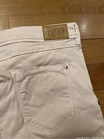 Close-up of back pocket and leather Biography Denim patch on pale denim jeans laid on wooden floor.