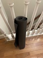 Rolled black yoga mat leaning against white banister on hardwood floor.