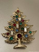 Front side of Christmas tree brooch showing gold-tone metal and multi-colored gemstones resembling ornaments