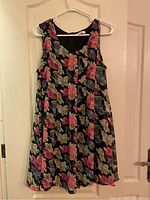 Front of floral sleeveless dress with large colorful flowers on black background hung on white hanger