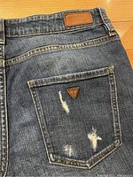 Back pocket detail showing brown leather Guess patch and metal logo with ripped denim.