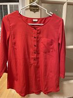 Red Jacqueline DeYong dress shirt hanging on a white hanger in front of a door, showing front buttons and chest pocket.