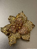 Front of gold tone flower brooch with layered petals, rhinestones reflect colors of Aurora Borealis.