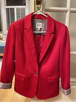 Red single-button blazer by Jules & Leopoldo hanging on a white hanger in good lighting. Shows front view, lapels, pockets, and brand label inside collar.