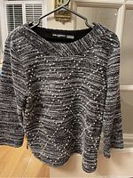 Black and white knit Karl Lagerfeld Paris sweater with pearl and lattice detailing hung on a hanger.