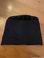 Front view of black fabric migraine relief cap laid flat showing smooth textile surface and slight texture changes.