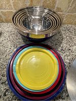 Stacked stainless steel mixing bowls nested inside each other with color-coded lids stacked separately beneath.