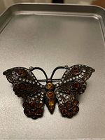 Front view of Nolan Miller butterfly brooch showing amber colored rhinestones and silver-tone metal wings.