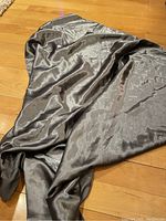 Image showing the full length and texture of the smoky grey silk scarf laid on a wooden floor, highlighting its shiny and smooth fabric.