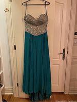 Full front view of turquoise ball gown hanging on a door, showing strapless bodice and full skirt.