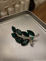 Front view of Weiss brooch showing green marquise-shaped gemstones and clear rhinestones on silver-tone metal base.