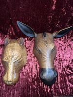 Two wooden animal head carvings, one zebra and one leopard, placed on a textured dark reddish fabric background.
