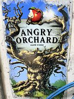 Metal advertising sign with Angry Orchard logo and artwork of snarling tree with apple.