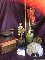 Wooden coffee grinder, Asian metal figurine, green glass vase with artificial flowers, and two decorative spherical objects against a purple draped background, ruler for scale.
