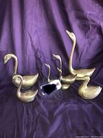 Seven solid brass bird figurines on a purple cloth background including six swans and one duck with a price tag attached to one swan.