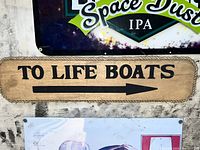 Photo showing the vintage wooden sign with the text 'TO LIFE BOATS' carved along with a right-pointing arrow, mounted on a wall.