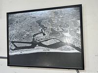Framed black and white aerial photograph showing Newport Beach Harbor and its surrounding area, taken in the 1940s, hung on a wall.