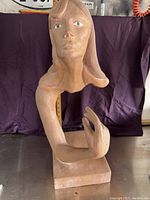 Front view of the Suspended Lady sculpture showing the bust, face, and hand gesture with green eyes and tan finish.