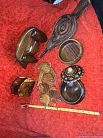 Photo showing full lot on red cloth background with wooden bellows, napkin holder, two wooden bowls, and six carved birds arranged. Measuring tape visible for scale.