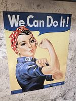 Metal sign mounted on a wall featuring the iconic 'We Can Do It!' image of a woman flexing her arm with text above her.