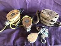 Lot of wooden and metal pulleys and yellow rope on a purple cloth.