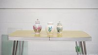 Front view of the three ceramic ginger jars displayed on a vintage yellow Formica table with metal legs against a white wall.