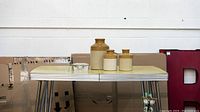 Three pottery jugs arranged by size with a glass candle holder on a small table.
